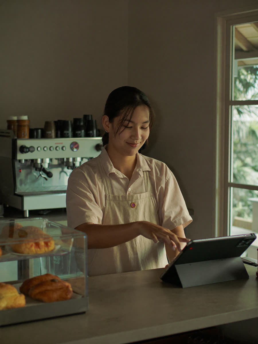 Filipino barista tapping a tablet behind the counter of a small coffee shop